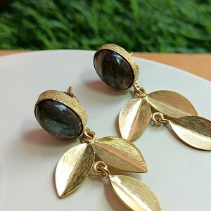 May include: A pair of gold earrings with a dark gray gemstone and gold leaf accents.