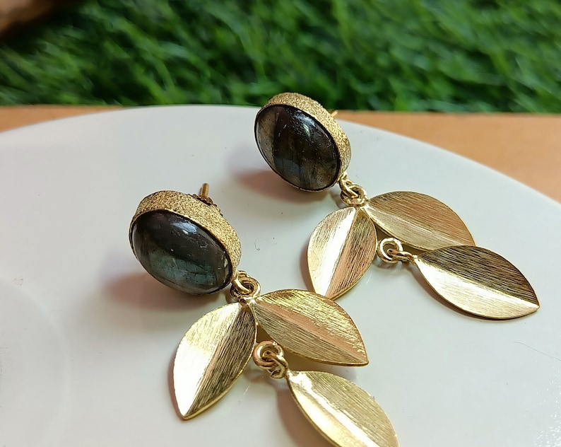May include: A pair of gold earrings with a dark gray gemstone and gold leaf accents.