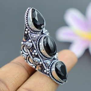 May include: A silver ring with three black gemstone accents. The ring has an ornate design with intricate details.