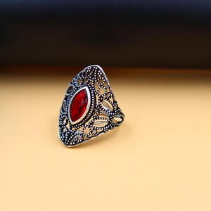 Op de afbeelding: Een zilveren ring met een rode edelsteen in een filigraan ontwerp.