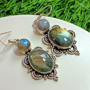Puede incluir: Un par de pendientes de plata con dos piedras de labradorita verde y azul iridiscentes engastadas en una filigrana de plata adornada.