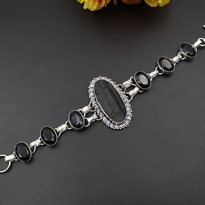 May include: A silver bracelet featuring a large oval black gemstone and smaller black gemstones on the chain.