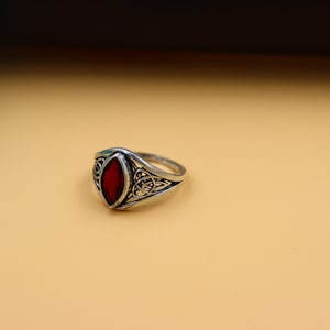 May include: A silver ring with a red gemstone set in a detailed design.