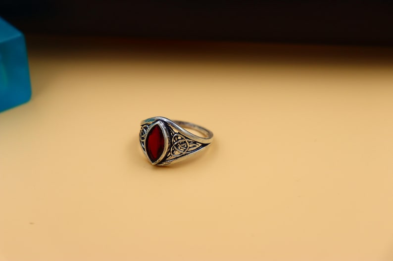 May include: A silver ring with a red gemstone set in a detailed design.