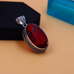 May include: A silver pendant with an ornate design and a large, red gemstone.