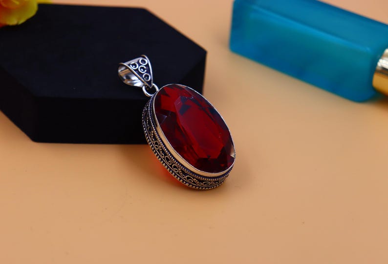 May include: A silver pendant with an ornate design and a large, red gemstone.