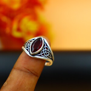 May include: A silver ring with a red gemstone set in a Celtic knot design.