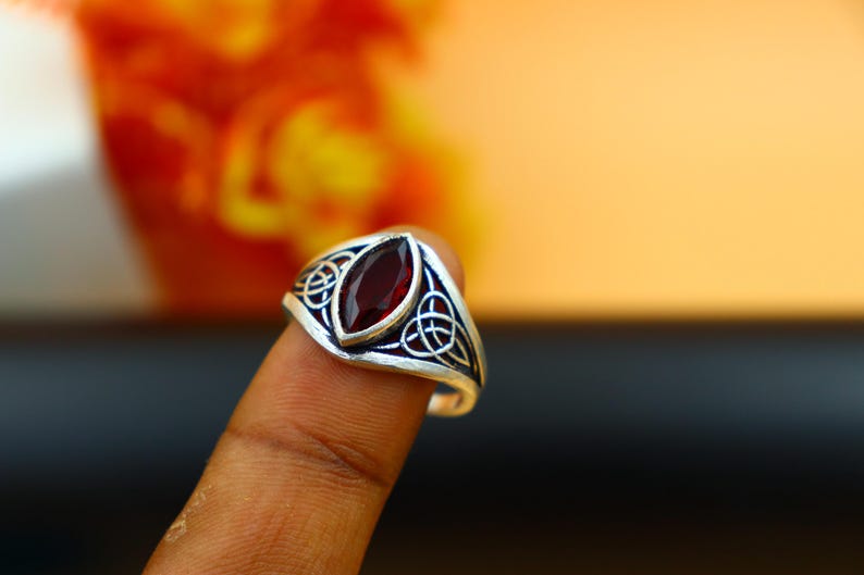 May include: A silver ring with a red gemstone set in a Celtic knot design.