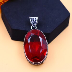 May include: A silver pendant featuring a large, oval-shaped, red gemstone. The pendant has a detailed, ornate design around the gemstone.