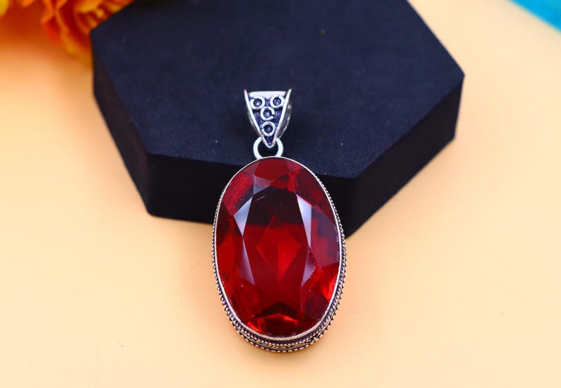 May include: A silver pendant featuring a large, oval-shaped, red gemstone. The pendant has a detailed, ornate design around the gemstone.