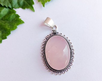 May include: A silver pendant with a delicate, ornate design features a large, oval-shaped, pale pink rose quartz gemstone.