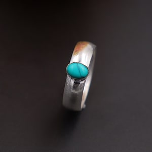 Op de afbeelding: Een zilveren ring met een turquoise steen in het midden.