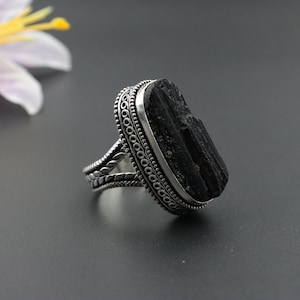 May include: A silver ring with a black tourmaline gemstone. The ring has a detailed, ornate design with a silver band.