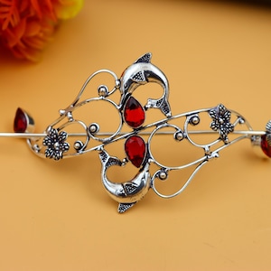 Puede incluir: Peine de pelo de plata con un delicado diseño floral y detalles de piedras preciosas rojas. El peine presenta dos figuras de delfines y es perfecto para añadir un toque de elegancia a cualquier peinado.