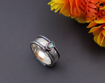 May include: A silver ring with a colorful gemstone set in the center. The ring has a textured band with a rope design.