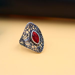 Op de afbeelding: Een zilveren ring met een rode edelsteen in een delicaat filigraan ontwerp.