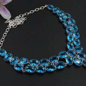 Op de afbeelding: Een zilveren ketting met een ontwerp van blauwe topaasstenen. De ketting heeft een ketting en een hanger met meerdere ovale stenen.