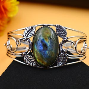 Puede incluir: Pulsera de plata con una gran piedra ovalada de labradorita engastada en un delicado diseño floral.