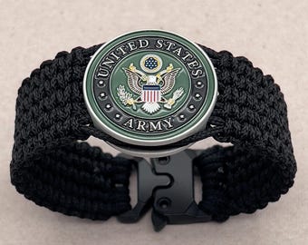 Könnte beinhalten: Schwarzes Paracord-Armband mit einem silbernen Metallverschluss und einem runden Emblem der US-Armee in Grün, Silber und Rot.