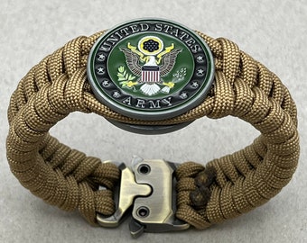 Könnte beinhalten: Ein braunes Paracord-Armband mit einem Metallverschluss und einem runden Metallanhänger mit dem Siegel der US-Armee. Das Siegel ist grün, gold und rot mit einem Weißkopfseeadler und den Worten "United States Army".
