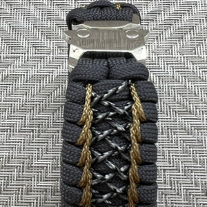 May include: A black paracord bracelet with gold and silver accents. The bracelet has a silver buckle closure.