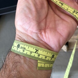 May include: A yellow measuring tape wrapped around a person's wrist. The tape reads "6" inches on one side and "7" inches on the other side. The tape is labeled "CHINA".