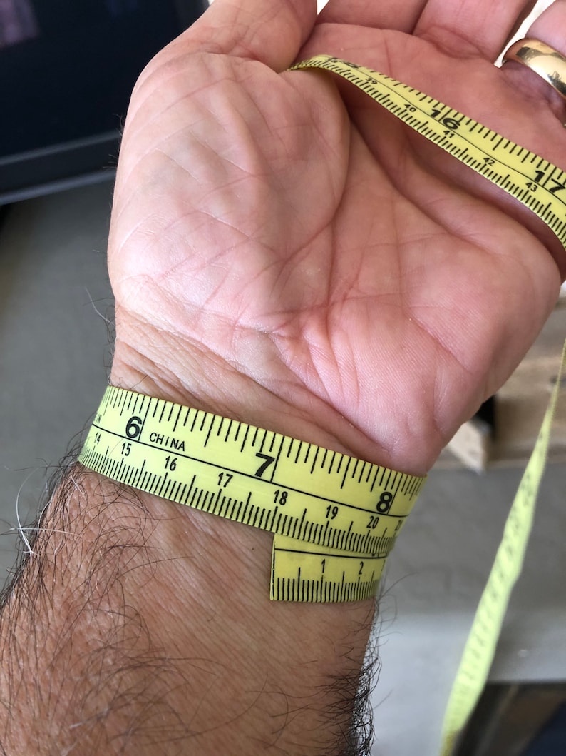 May include: A yellow measuring tape wrapped around a person's wrist. The tape reads "6" inches on one side and "7" inches on the other side. The tape is labeled "CHINA".
