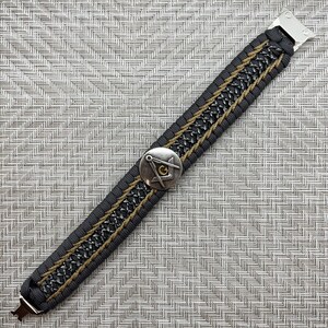 May include: A black and gold paracord bracelet with a silver metal clasp and a silver and gold compass charm.