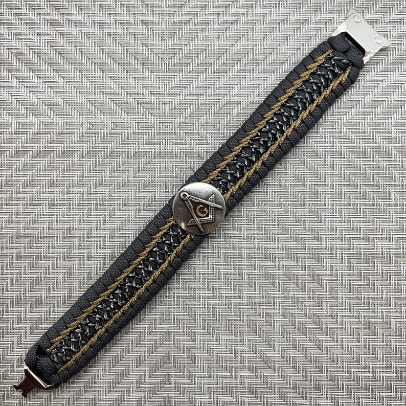 May include: A black and gold paracord bracelet with a silver metal clasp and a silver and gold compass charm.