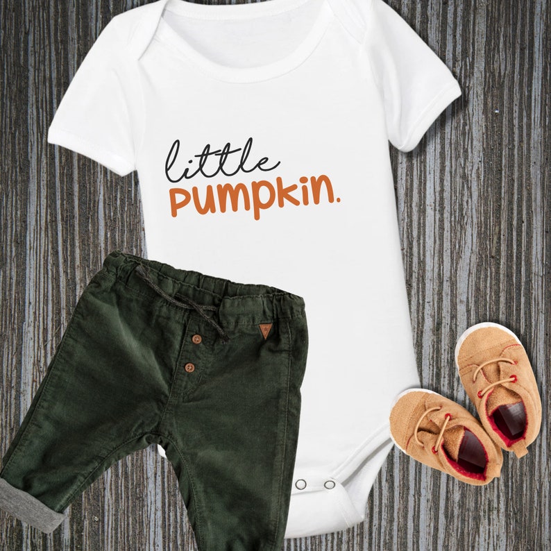 May include: White baby onesie with the text "little pumpkin" in black and orange. Green corduroy pants and brown shoes are also pictured.