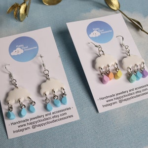 May include: A pair of white cloud earrings with colourful raindrops hanging from them. The earrings are handmade and come with a card that says "Handmade jewellery and accessories - www.happycloudacc.etsy.com Instagram: @happycloudaccessories".