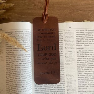 Könnte beinhalten: Ein braunes Leder-Lesezeichen mit dem Text "Sei stark und mutig. Hab keine Angst. Lass dich nicht entmutigen. Denn der Herr, dein Gott, ist mit dir, wohin du auch gehst. Josua 1,9"