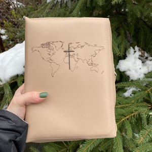 May include: A beige leather bible cover with a world map and a cross design embossed on the front.