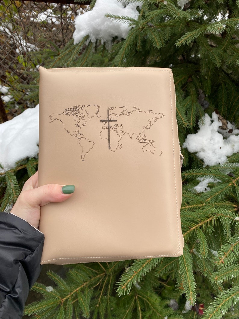 May include: A beige leather bible cover with a world map and a cross design embossed on the front.