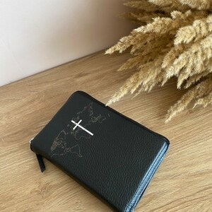 May include: A black leather zippered journal with a world map and a white cross design.
