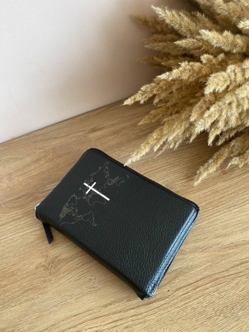 May include: A black leather zippered journal with a world map and a white cross design.
