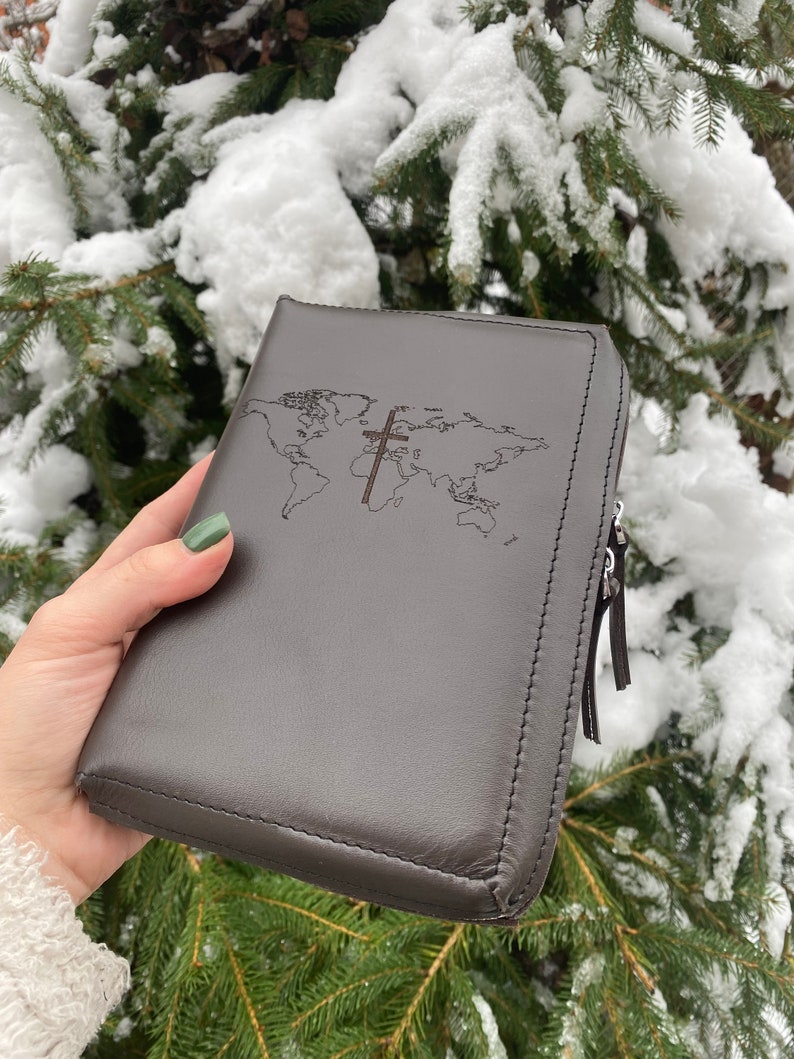 May include: A brown leather zippered Bible cover with a world map and a cross design.