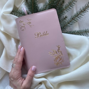 Op de afbeelding: Een roze lederen gebonden Bijbel met gouden bloemmotieven en het woord "Bijbel" in reliëf op de voorzijde.