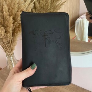 May include: Black leather zippered travel wallet with a world map and cross embossed on the front.
