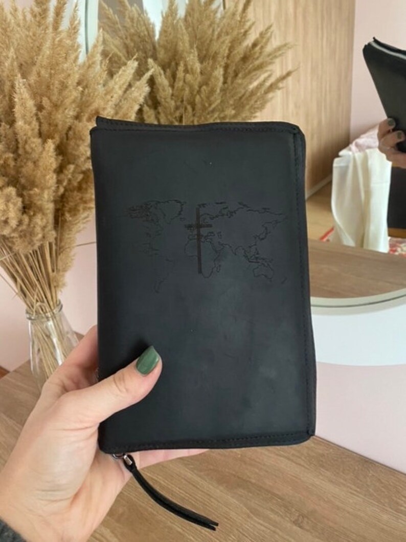May include: Black leather zippered travel wallet with a world map and cross embossed on the front.