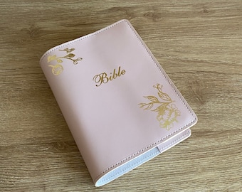 May include: A pink leather Bible cover with gold floral designs and the word "Bible" embossed in gold.