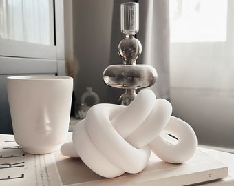 May include: White ceramic knot sculpture on top of a stack of books. The top book is titled "Cereal 18" and the bottom book is titled "corey lee".