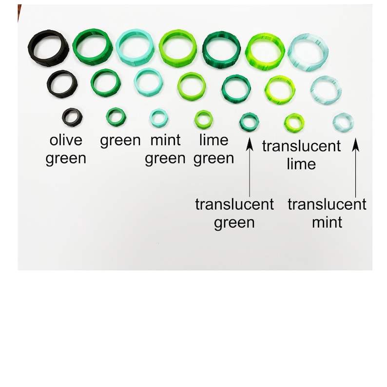 May include: A collection of various green-toned rings, including olive, green, mint green, lime green, translucent green, and translucent lime. The rings vary in size and shade, arranged on a white surface with labels identifying each color.