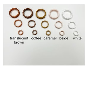 May include: A collection of wooden rings in various sizes and colors, including translucent brown, coffee, caramel, beige, and white. The rings are arranged in rows, with the color names displayed below.