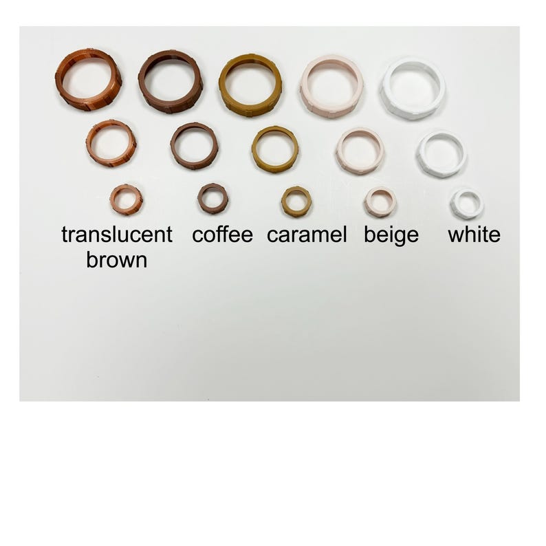 May include: A collection of wooden rings in various sizes and colors, including translucent brown, coffee, caramel, beige, and white. The rings are arranged in rows, with the color names displayed below.