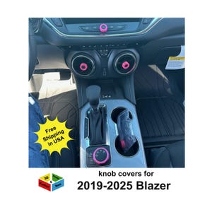 May include: Interior view of a car dashboard with pink knob covers installed. The image shows the air vents, gear shift, and center console. Text on the image reads "knob covers for 2019-2025 Blazer."