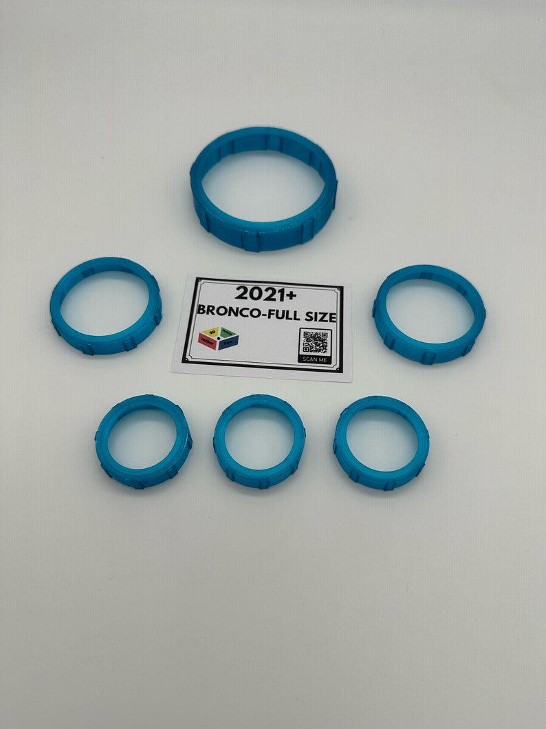 May include: Several turquoise-colored, circular objects with a ridged design are arranged on a white surface. A rectangular card with the text "2021+ BRONCO-FULL SIZE" is also present, along with a QR code.