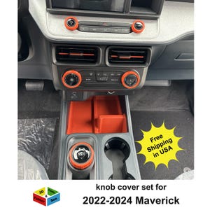 May include: Orange knob cover set for a 2022-2024 Maverick vehicle. The set includes covers for the dashboard knobs, gear shift, and storage compartments. The interior is gray and black.