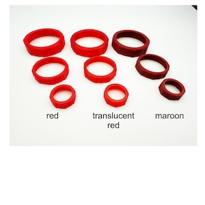 May include: An assortment of red, translucent red, and maroon rubber rings of varying sizes. The rings are arranged on a white surface, with text labels identifying the colors. The rings appear to be made of a flexible material.