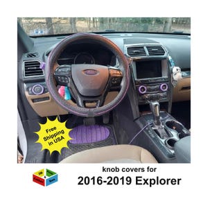 May include: Interior view of a Ford Explorer with a black steering wheel cover with pink stitching. The dashboard features purple accents, including knob covers and floor mats. Text reads "knob covers for 2016-2019 Explorer."
